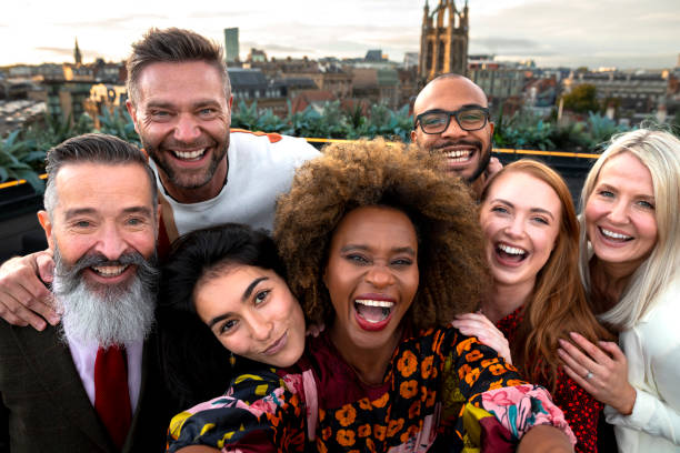Work Party Selfie A wide selfie shot of a multiracial group of friends at a rooftop bar in Newcastle Upon Tyne. They are looking at the camera, smiling and laughing. office parties stock pictures, royalty-free photos & images