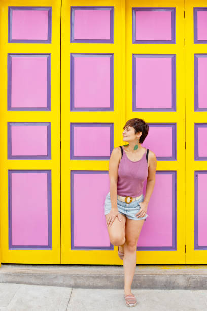 vue de face recadrée d’une femme debout contre un mur décoré de motifs rectangulaires jaunes et roses. - pink buildings photos et images de collection