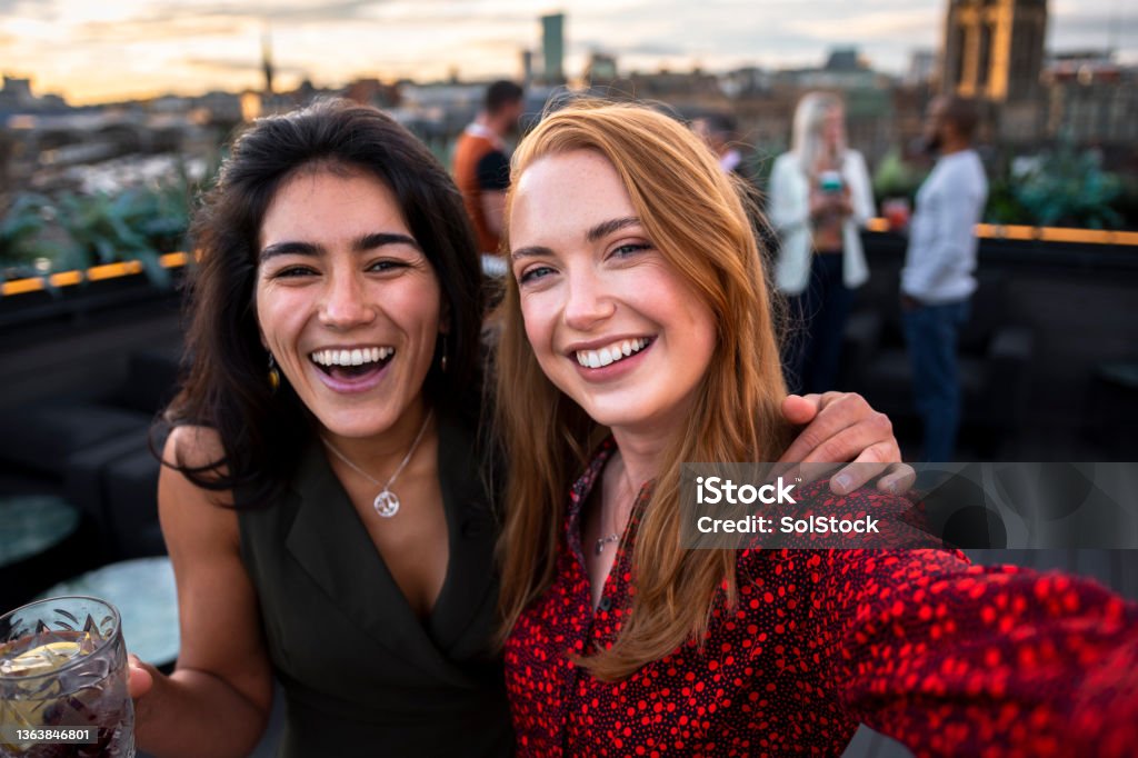 Rooftop Party Selfie A selfie shot of two female friends at a rooftop bar in Newcastle Upon Tyne. They are looking and smiling at the camera with cocktails in hand. There are people talking and drinking in the background. Friendship Stock Photo
