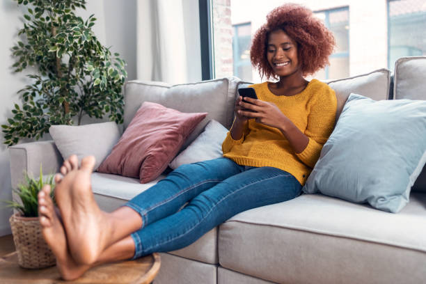 istock Confident young woman using her mobile phone while sitting on sofa at home. 1363850976