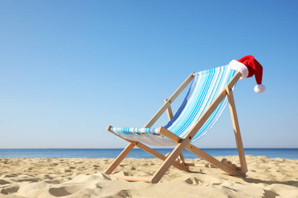 istock Deck chair with Santa Claus hat on sandy beach. Christmas vacation 1363852214