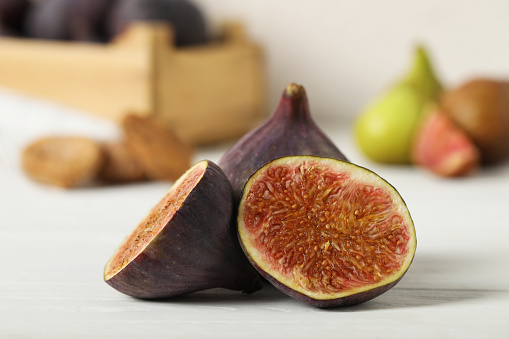 Tasty raw cut and whole figs on white table, closeup