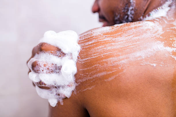 brazilian man washing body with shower sponge in white bathroom stock photo