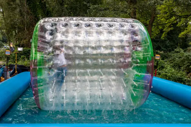 Photo of Water or aqua zorbing. Children play inside the inflatable transparent roller floating in swimming pool. Water walking or zorbing very popular fun activity and suitable for all ages.