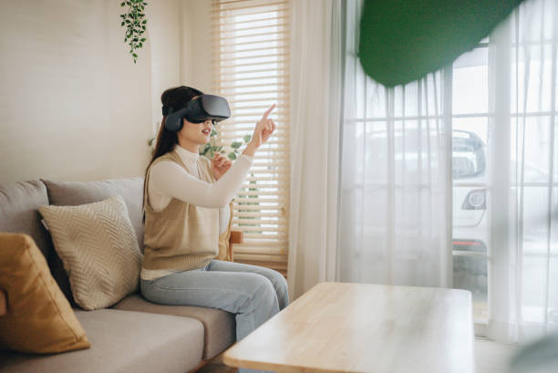 Attractive young Asian woman wearing VR Glasses sitting on sofa at home. stock photo