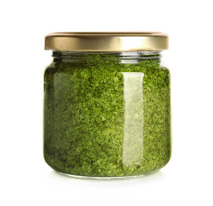 Jar of tasty arugula pesto on white background