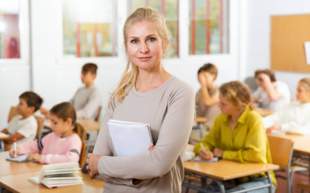 Portrait of positive female school teacher Portrait of positive female school teacher posing in classroom with her pupils on background 12 13 years pre adolescent child female blond hair stock pictures, royalty-free photos & images