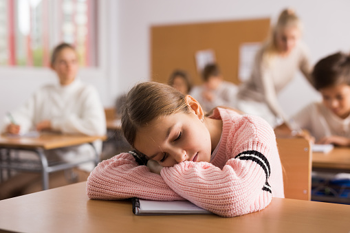 Portrait of tired school girl lying and sleeping at desk in classroom during lesson