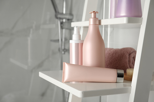 Diferentes productos para el cuidado del cabello y toalla en estanterías en el baño photo