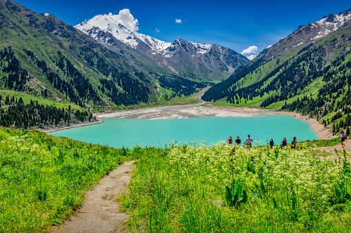 People hike at Big Almaty Lake in the Ile Alatau Mountains near Almaty, Kazakhstan on a sunny day.