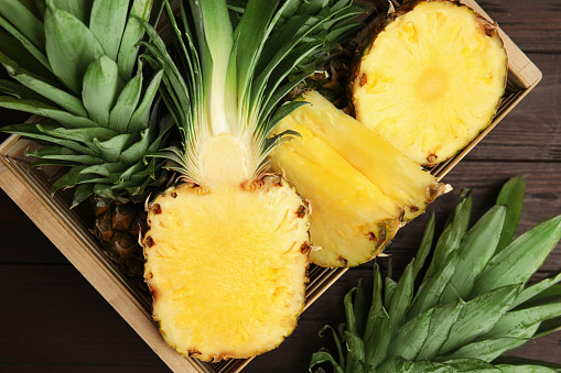 Tasty cut pineapples in crate on wooden table, flat lay