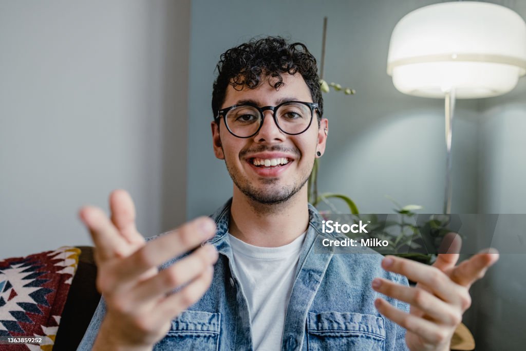 Young man talking on a video call and looking at the camera Portrait of a young man at home relaxing and using headphones Talking Stock Photo