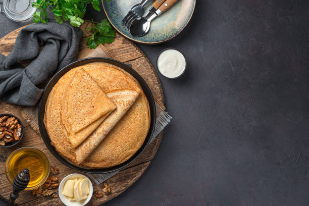 Stack pancakes on a dark background with honey, sour cream and nuts. Russian blini