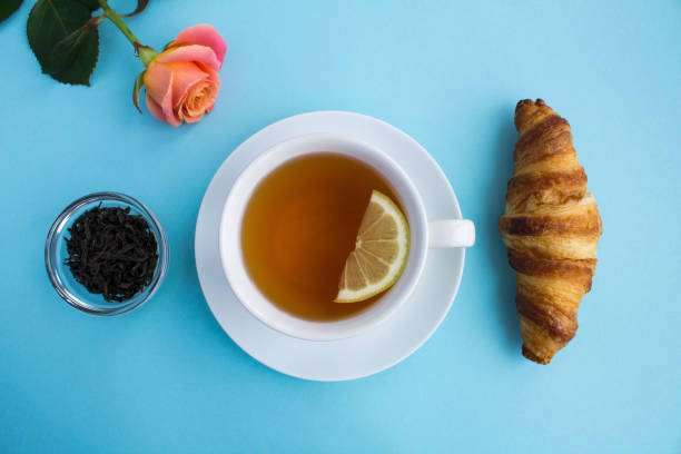 istock Tea cup, croissant and pink rose on the blue  background. Top view. Copy space. 1363860426