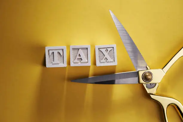 Photo of wood block with alphabet TAX and scissors on yellow background