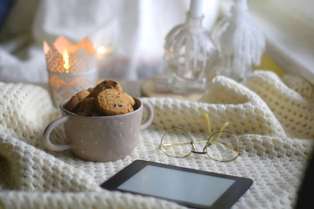 Tablet, Glasses, Cookies and Blanket Bowl of chocolate chip cookies, digital tablet, reading glasses, soft blanket and lit candle. Hygge at home. Selective focus. comfort food stock pictures, royalty-free photos & images