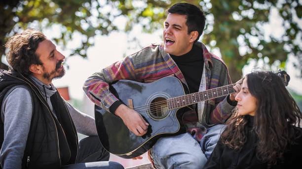 istock Friends play guitar and singing together while sitting on bench 1363862731