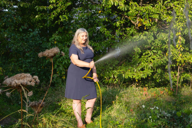 maturo donna irrigazione giardino - women large build gardening outdoors foto e immagini stock