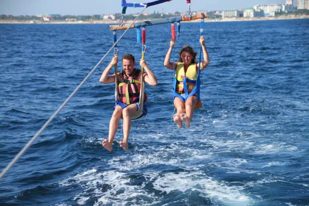 Happy couple Parasailing on Beach in summer. two people under parachute hanging in air above sea surface