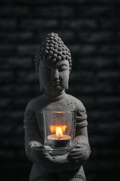 istock Closeup stone Buddha sculpture on black background, with burning candle. 1363868570