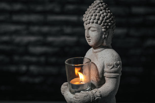istock Closeup stone Buddha sculpture on black background, with burning candle. 1363868602