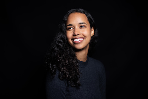 Studio portrait of a happy young latin american woman on black background. Woman in black tshirt looking away and smiling.