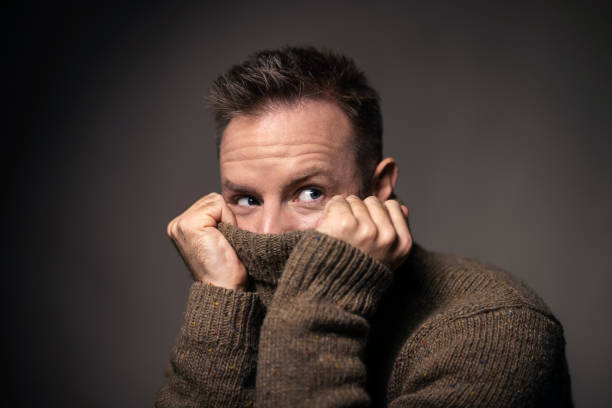 Young man covering face with turtleneck sweater Close-up of a young man pulling a sweater over his face. Man covering face with a turtleneck sweater and looking away against grat background. sheepish look stock pictures, royalty-free photos & images