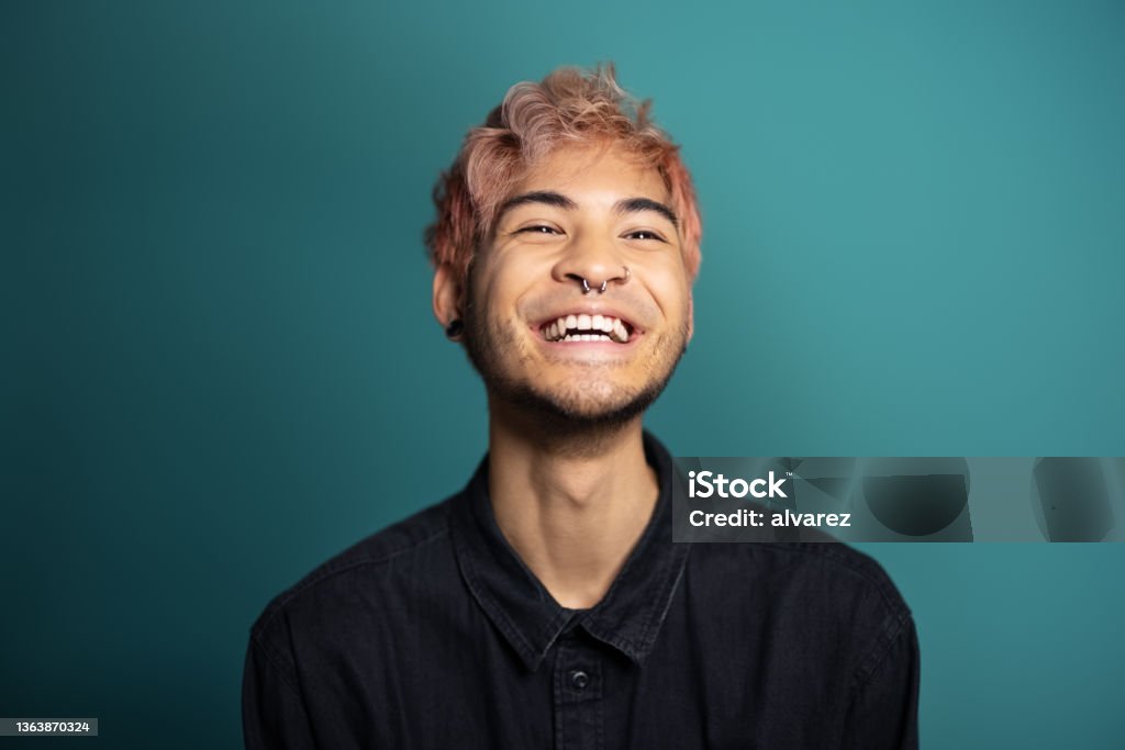 Cheerful young man smiling on blue background Cheerful young man smiling on blue background. Portrait of an asian man with pink hair and piercing in the studio. Men Stock Photo