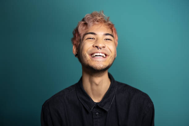 Cheerful young man smiling on blue background Cheerful young man smiling on blue background. Portrait of an asian man with pink hair and piercing in the studio. pink hair stock pictures, royalty-free photos & images