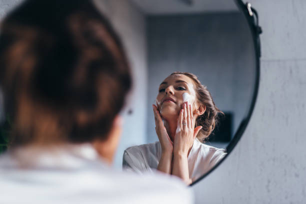 Woman applies cleansing foam to her face while caring for her skin. stock photo