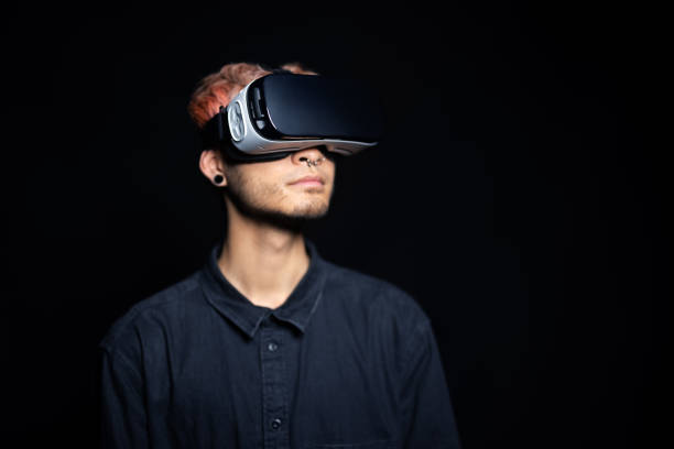 Close-up of young man using virtual reality glasses on black background. Asian man wearing VR simulator headset on studio background.