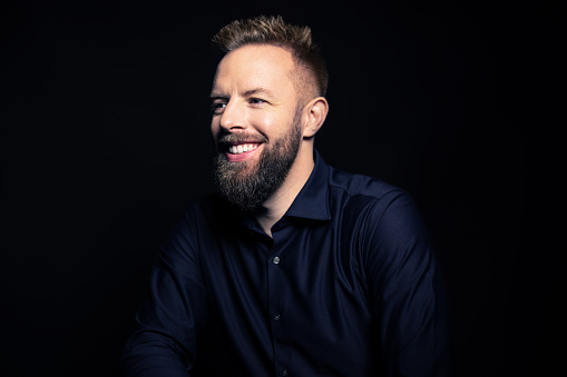 Happy young man with beard looking away and smiling. Handsome young man on black background