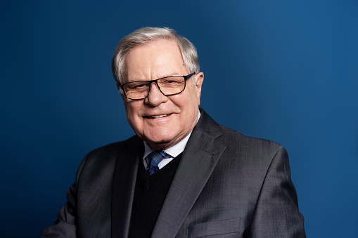Smiling senior businessman with glasses looking at camera on blue background. Portrait of a mature businessman in studio.