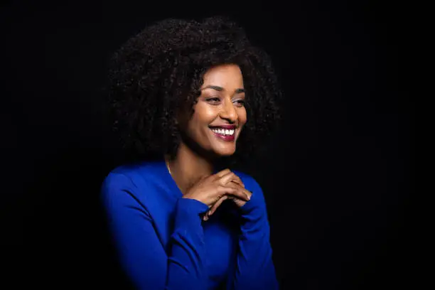 Smiling african woman with curly hair looking away against black background. Mid adult woman in casuals looking at copy space.