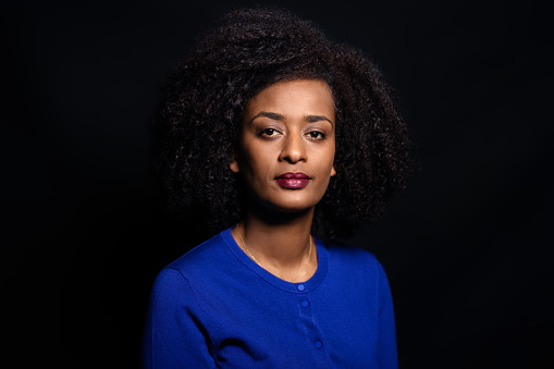 Studio portrait of a confident african american woman looking at camera. Mid adult female with short curly hair against black background.