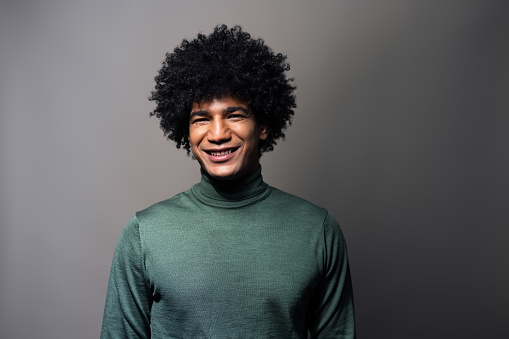 Studio portrait of a handsome young man on gray background. North african man with afro hairstyle smiling at camera.