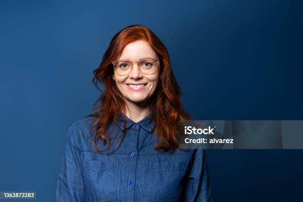 Portrait Of A Smiling Mature Woman With Red Hair On Blue Studio Background Stock Photo - Download Image Now