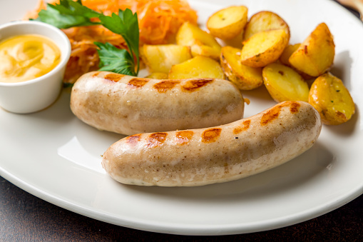 bavarian sausages with potatoes and fried cabbage on plate on dark brown concrete table close up