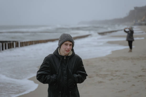 istock frozen young man stands on the seashore in a warm hat and winter jacket 1363872541