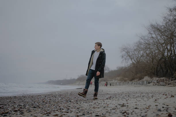 istock a young man in warm clothes walks along the cold sandy seashore 1363873199