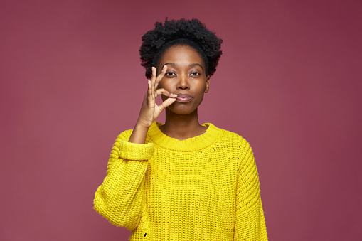Stylish african american young woman hold fingers near lips show be quiet gesture, promise to keep secret private information, ask silence. High quality photo