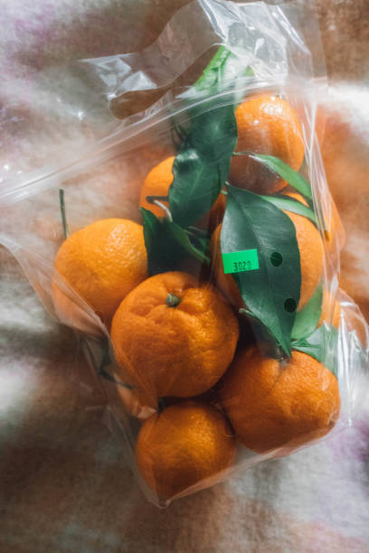 plastic bag of mandarins from the fruit stand with green sticker sitting on soft pink peach wool blanket