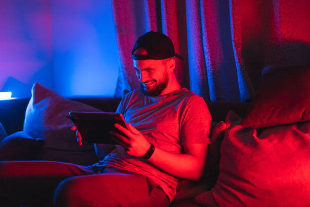 istock Young bearded happy man using his tablet for gaming with RGB lights in the background while relaxing at home 1363882009