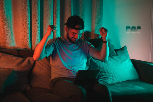 istock Young bearded happy man using his tablet with RGB lights in the background while casually working from home 1363882034