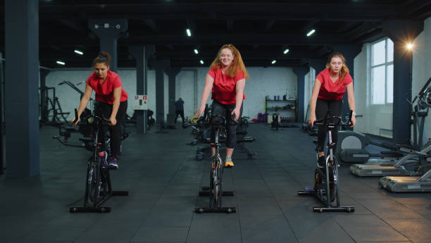 gruppo caucasico sano di donne che esercitano l'allenamento sulla cyclette della macchina da ciclismo in palestra - spinning health club instructor gym foto e immagini stock