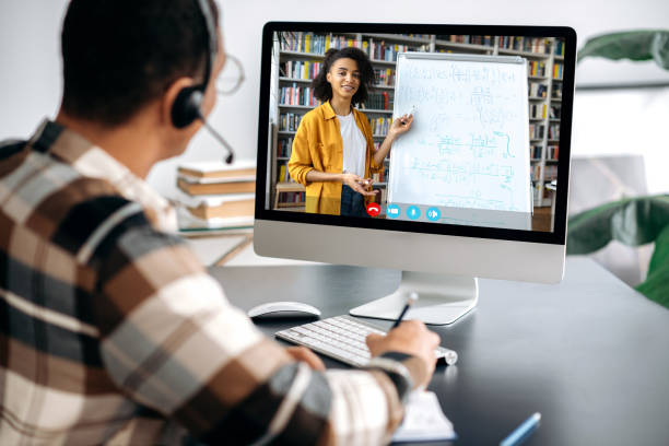istock E-learning concept, webinar, online lecture. Over shoulder view of male student on a computer screen, female friendly african american teacher on the screen conducts an online lesson,a guy takes notes 1363885042