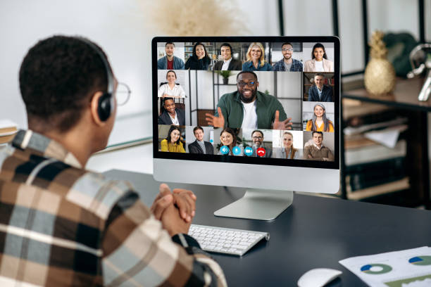 istock Online video communication. View over a man's shoulder on a computer screen with multiracial people, communicating by video call, a group of partners discuss a project, distant business meeting 1363885047
