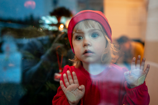 Sad Little girl wearing red hood riding costume photographed through the window