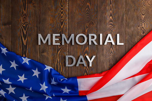 the words memorial day laid with silver metal letters on wooden board surface with crumpled usa flag.