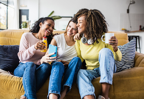 Cheerful multiracial female friends enjoying free time together at home - Three happy young adult women hanging out while - Friendship and social gathering concept